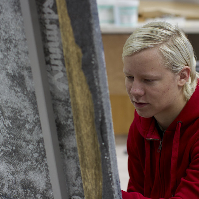 Hér er Alexander að mála fjallasýn úr Siglufirði á efni utan af húsgögnum. (Ljósmynd: Lára Stefánsdóttir)