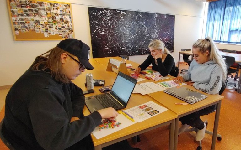 Björn Ægir sorterar einbeittur gotterí eftir litum. Handan borðsins eru Elísabet og Viktoría. 
Ljós…